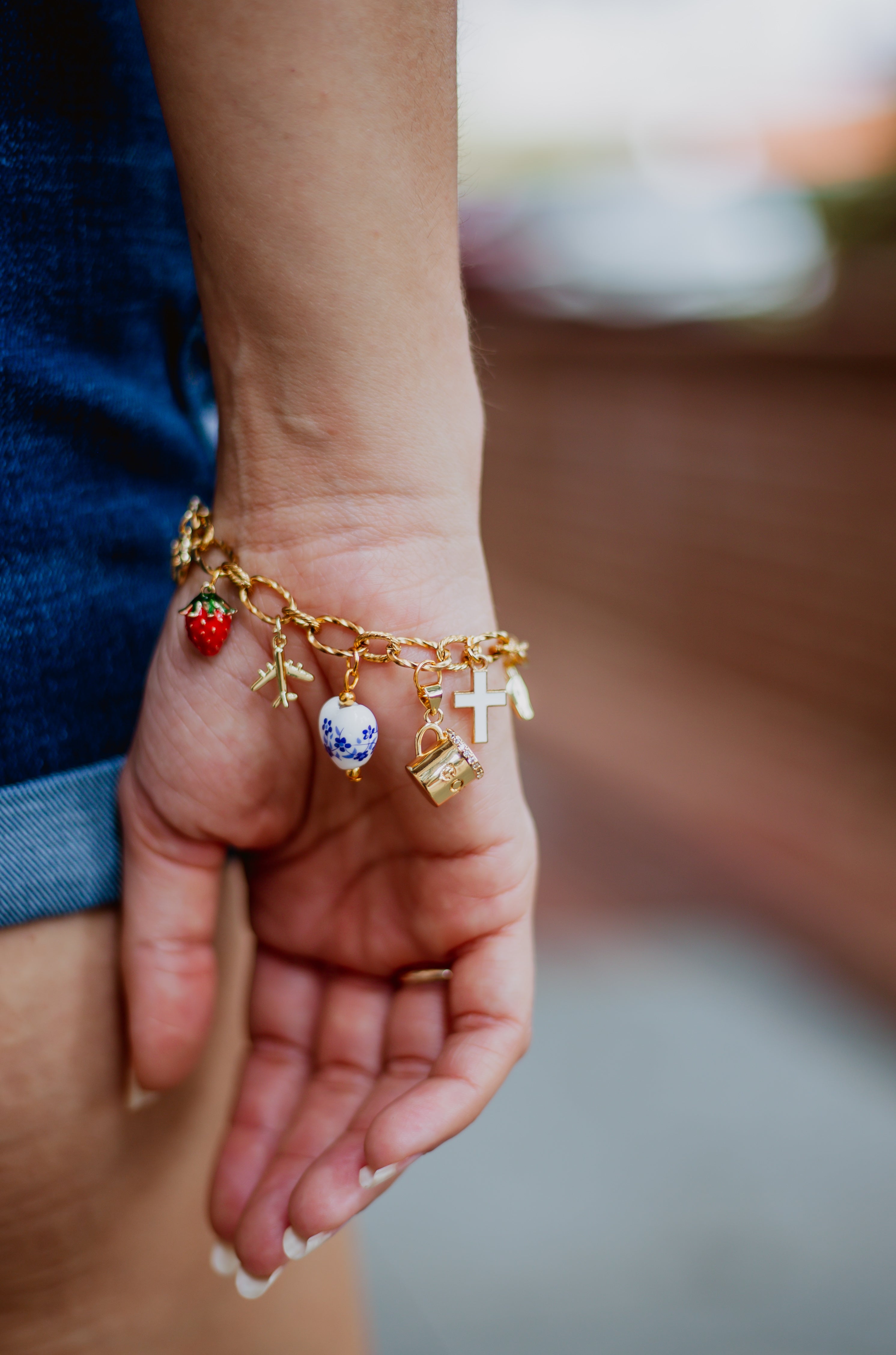 Hand wearing a gold charm bracelet with various charms against a blurred background