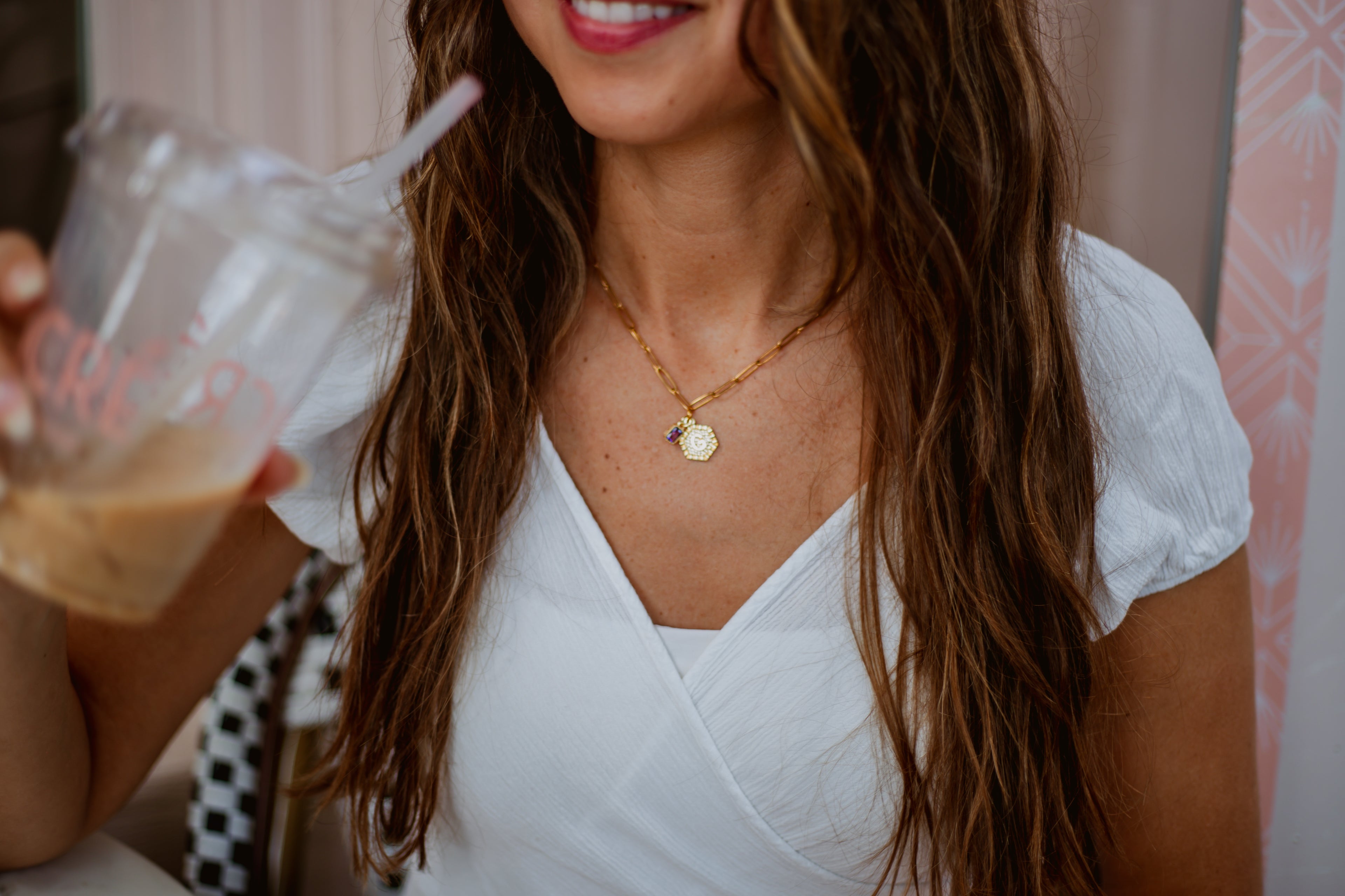 Woman in a white dress holding a drink with a straw, wearing a necklace.