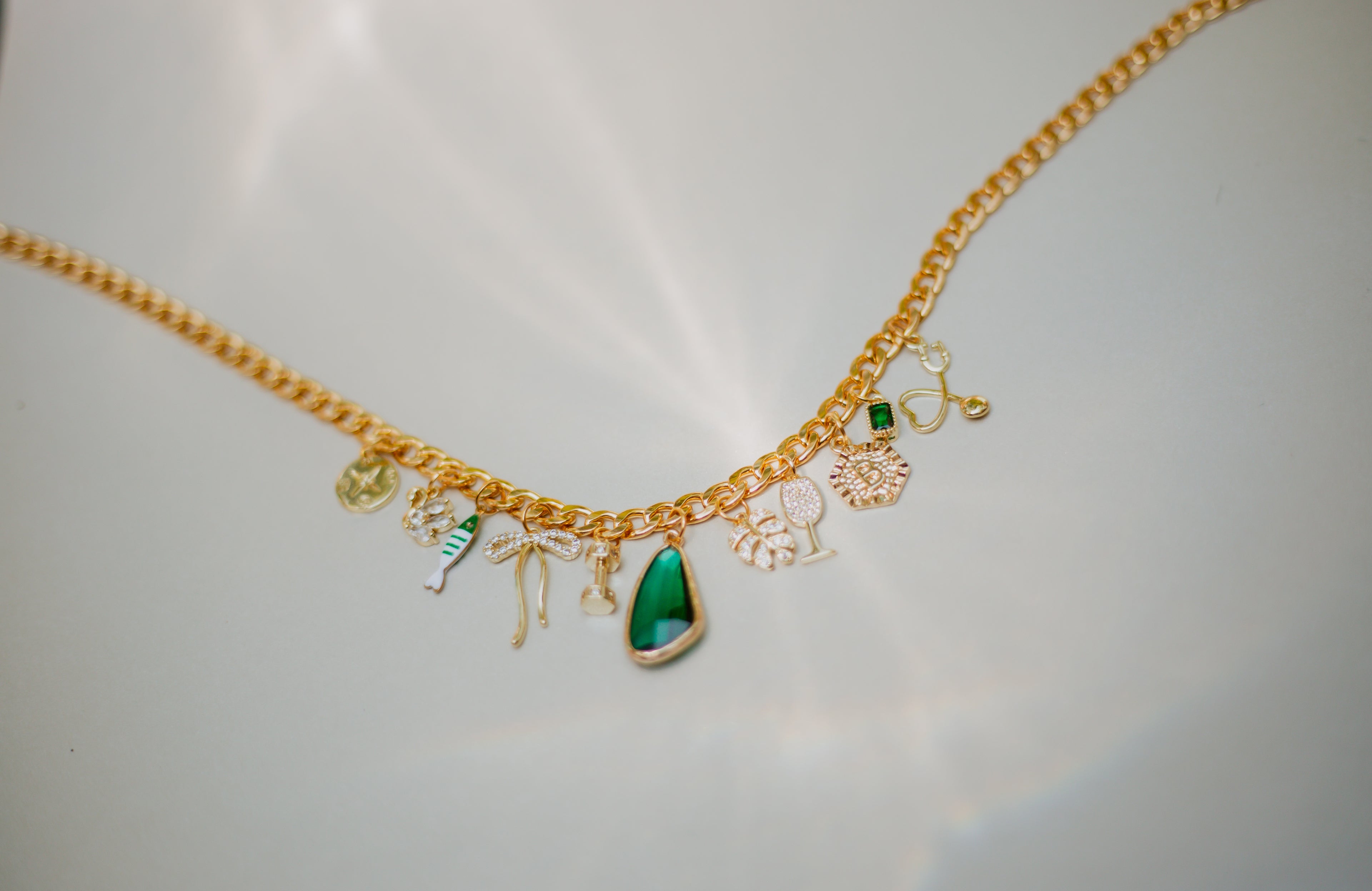 Gold necklace with various charms on a light gray background